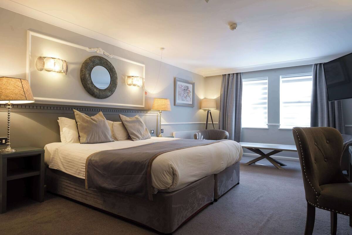 A hotel room with a large bed, bedside lamps, a round mirror, and a TV.
