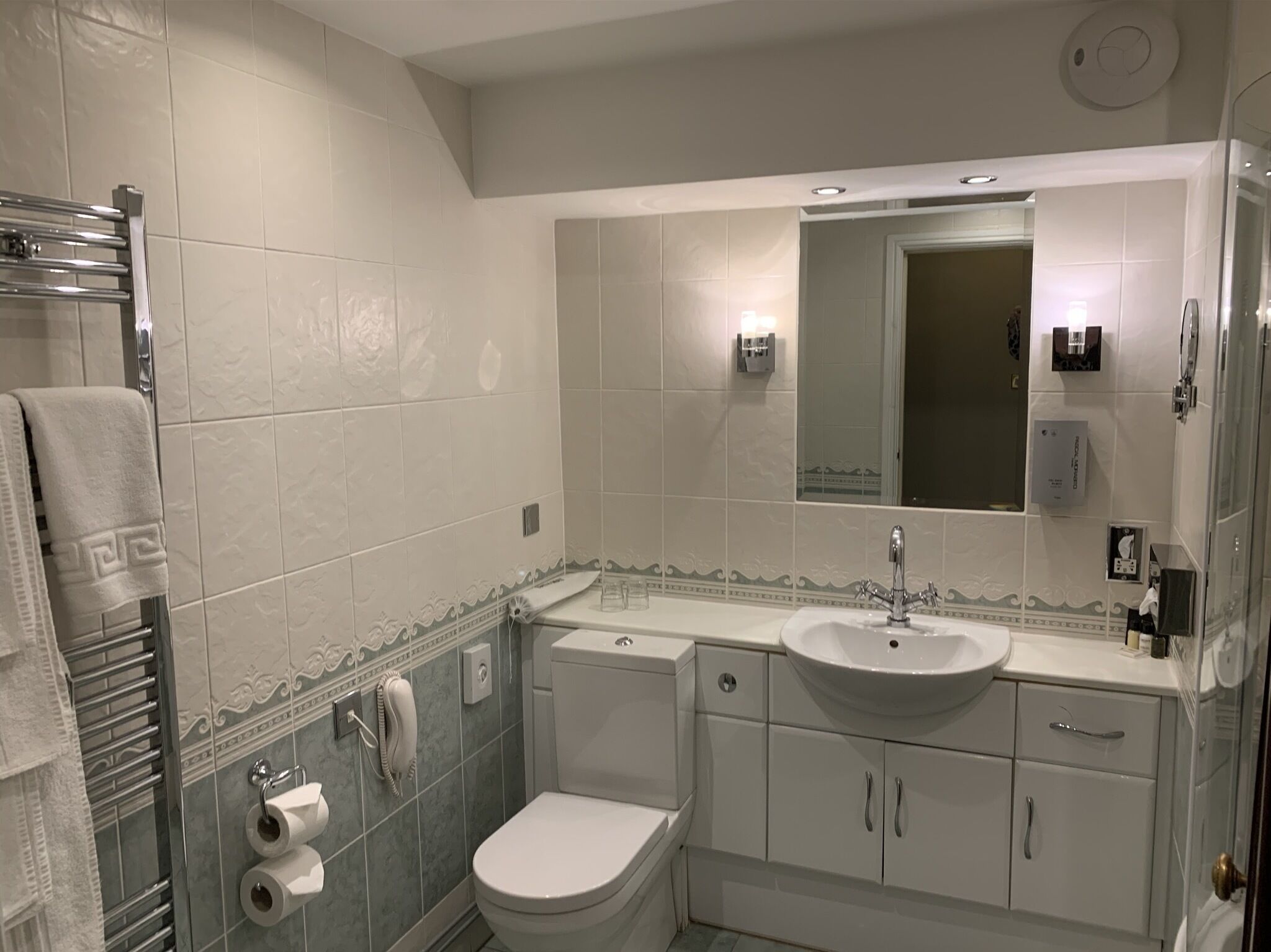 A modern bathroom with a toilet, sink, and mirror. There is a towel rack with a towel hanging on it.