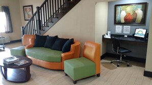 A modern living room with a green and orange sofa set, a small round table, a desk with a computer, and a staircase. - Days Inn by Wyndham Ashland (Ashland)