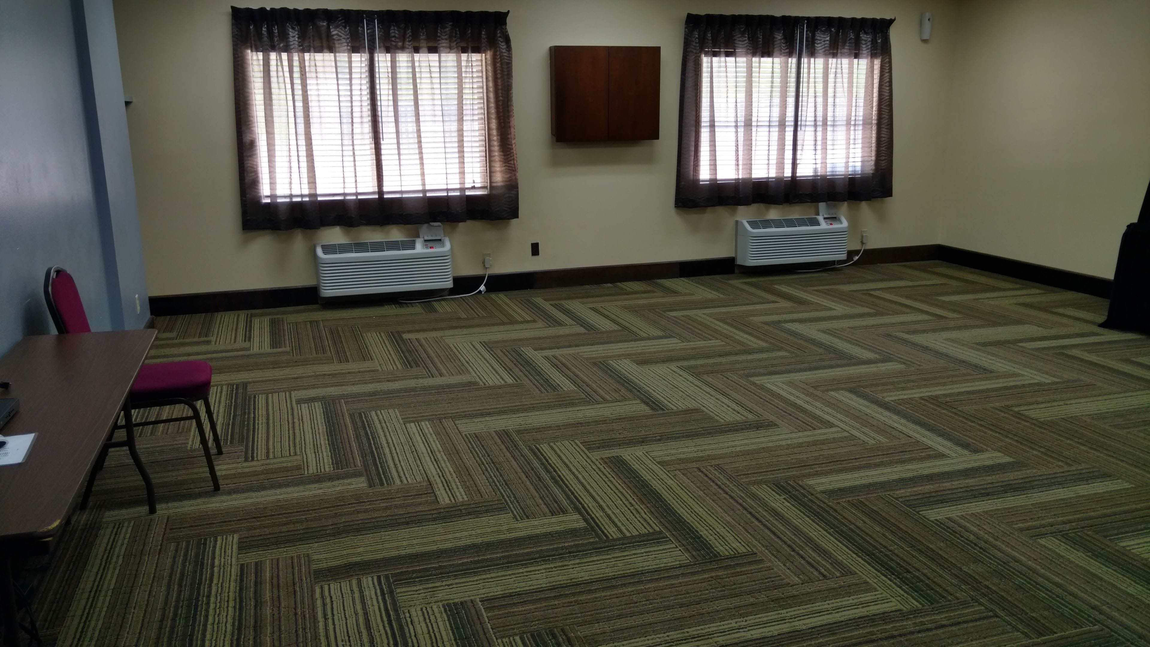 Una sala de conferencias con dos ventanas, suelo alfombrado, una mesa con sillas y dos equipos de aire acondicionado instalados en la pared.