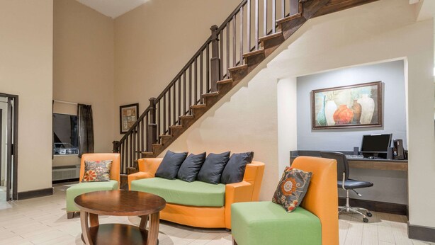 A spacious living area with a wooden staircase, a green and orange sofa set, a round coffee table, and a desk with a computer. - Days Inn by Wyndham Ashland (Ashland)