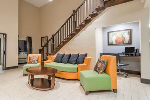 A spacious living area with a wooden staircase, a green and orange sofa set, a round coffee table, and a desk with a computer. - Days Inn by Wyndham Ashland (Ashland)