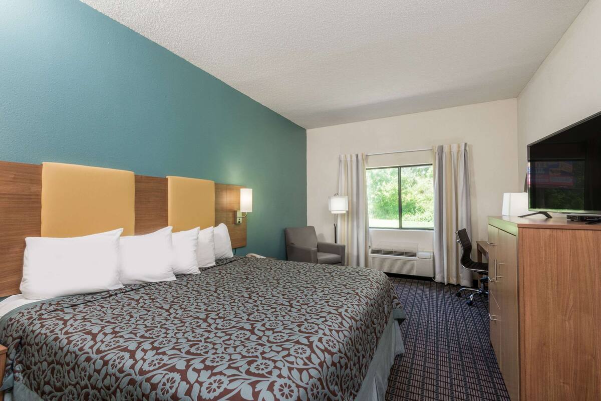 A hotel room with a large bed, a desk with a computer, a TV, and a window with curtains.
