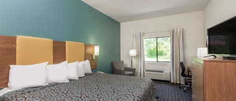 A hotel room with a large bed, a desk with a computer, a TV, and a window with curtains.