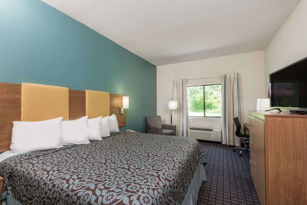 A hotel room with a large bed, a desk, a chair, a television, and a window with curtains.