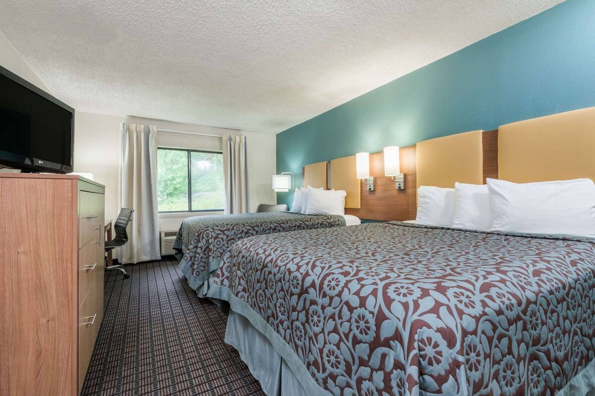 A hotel room with two beds, a desk, a TV, and a window with curtains.