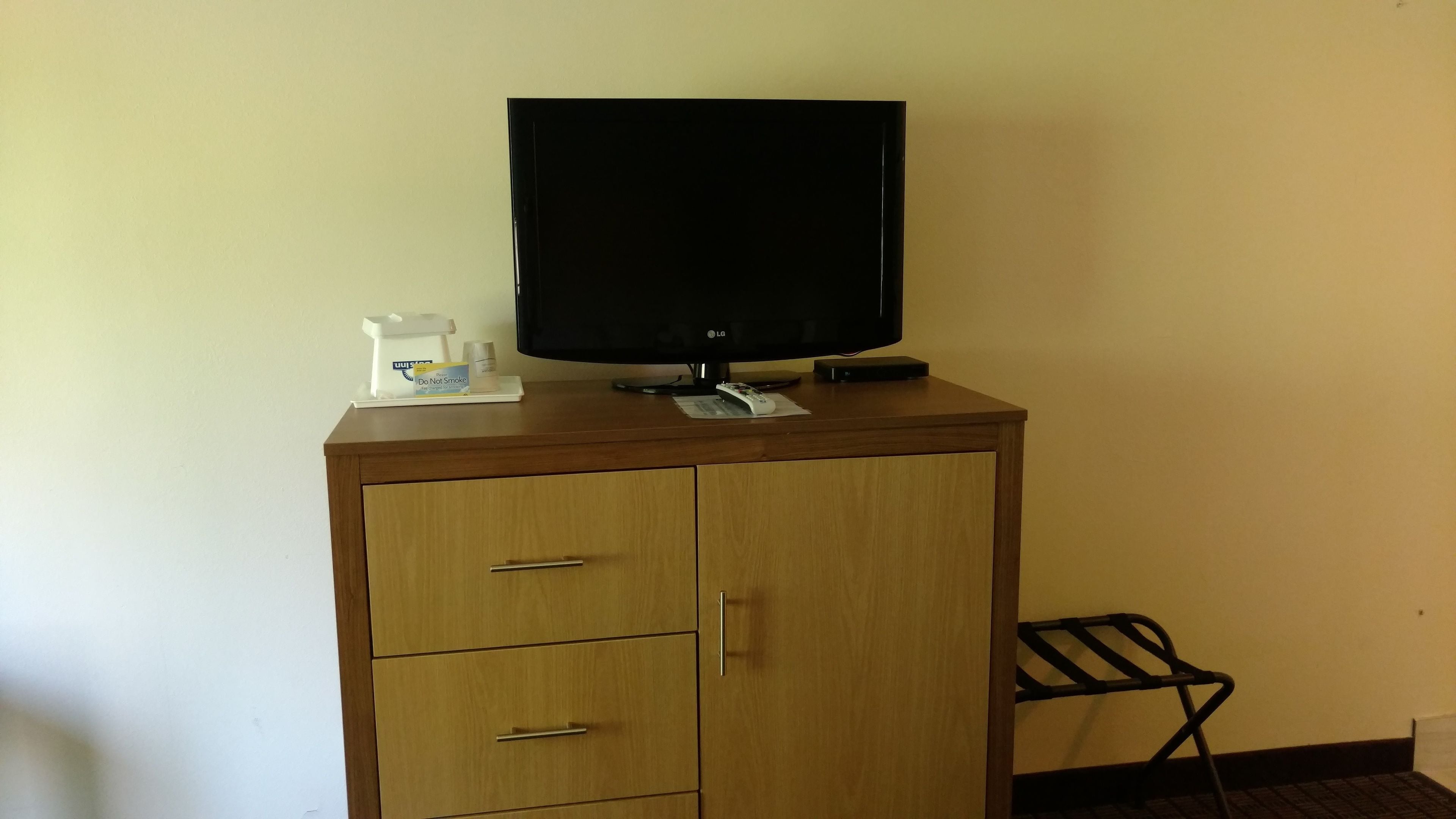 Un meuble en bois sur lequel est posée une télévision à écran plat, une télécommande et un petit plateau avec une machine à café et un panneau indiquant « Il est interdit de fumer ».