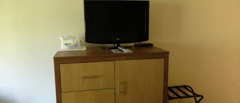 A wooden cabinet with a flat-screen TV on top, a remote control, and a small tray with a coffee maker and a 'Do Not Smoke' sign.