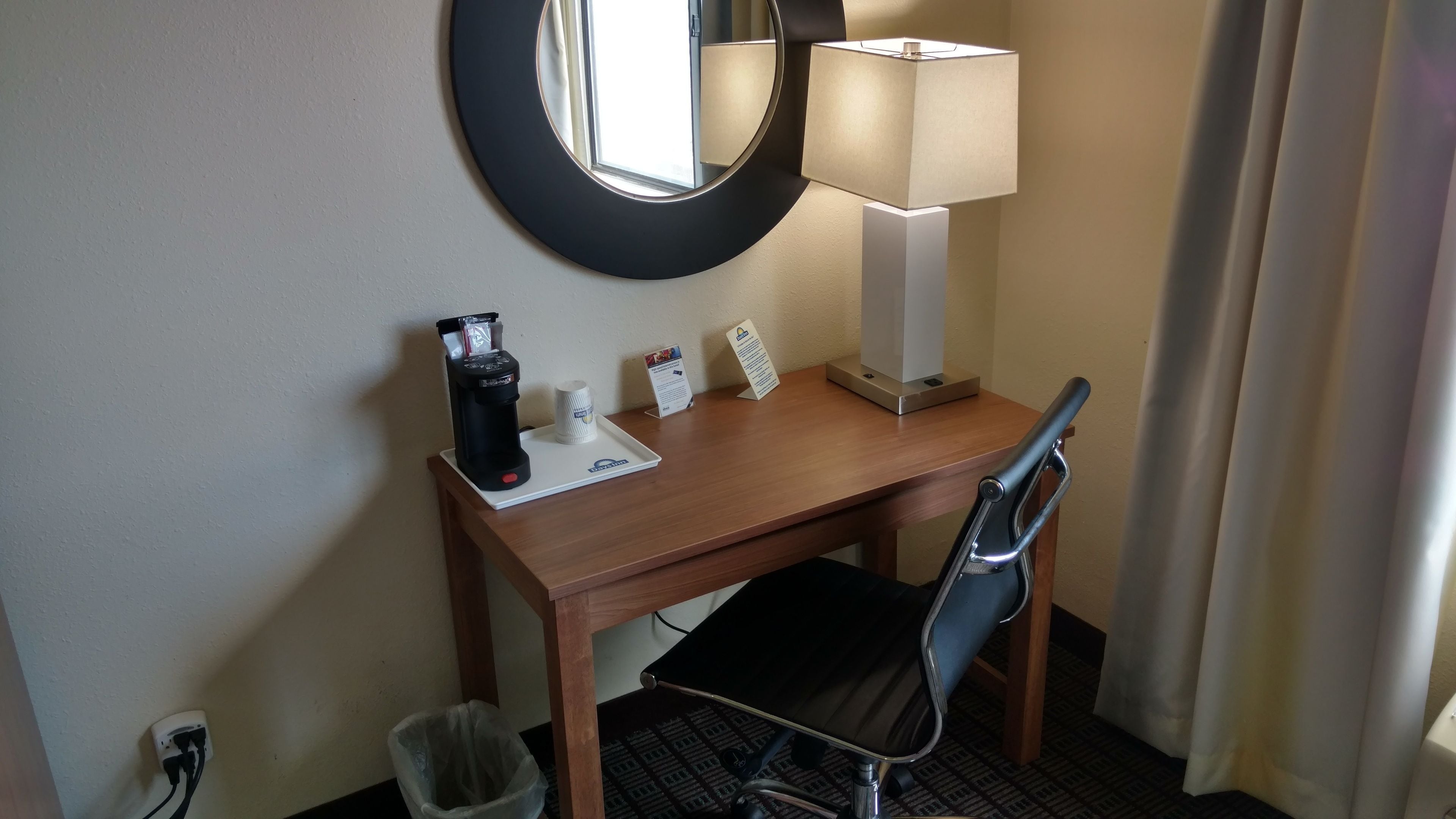 Un bureau dans une chambre d’hôtel, avec une machine à café, une lampe, une poubelle et une chaise.