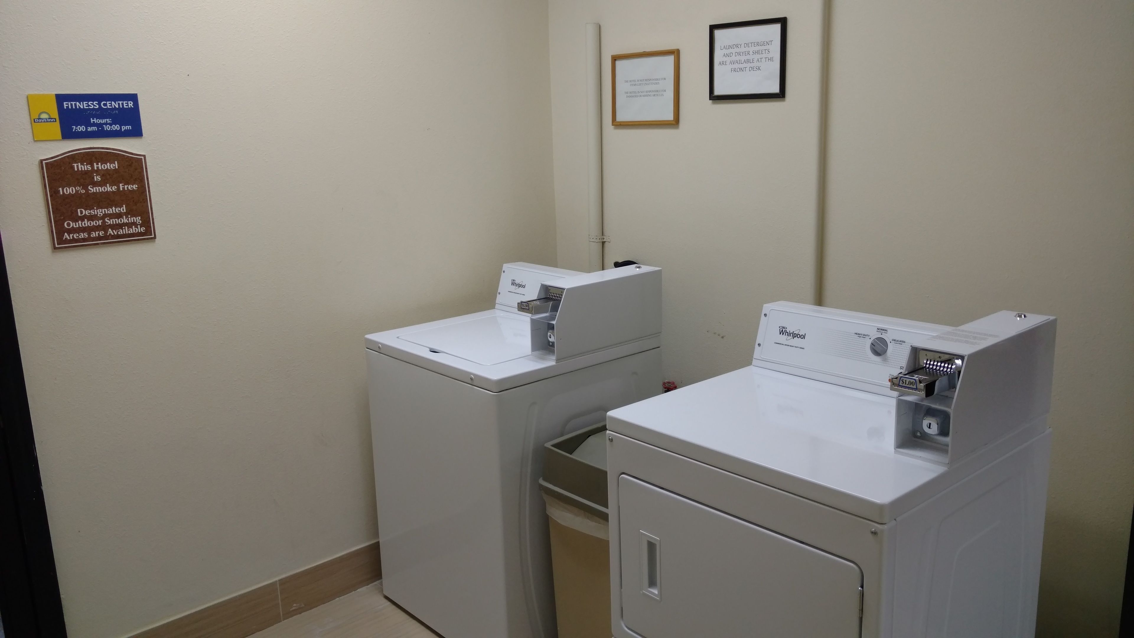 A laundry room with two Whirlpool washers and dryers, a fitness center sign, and a smoke-free hotel sign.