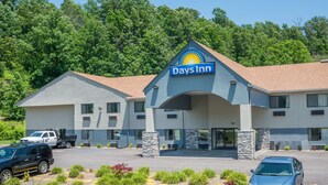 A Days Inn with a modern design, featuring a prominent sun logo, a parking lot with several cars, and a landscaped area with plants and decorative stones. - Days Inn by Wyndham Ashland (Ashland)