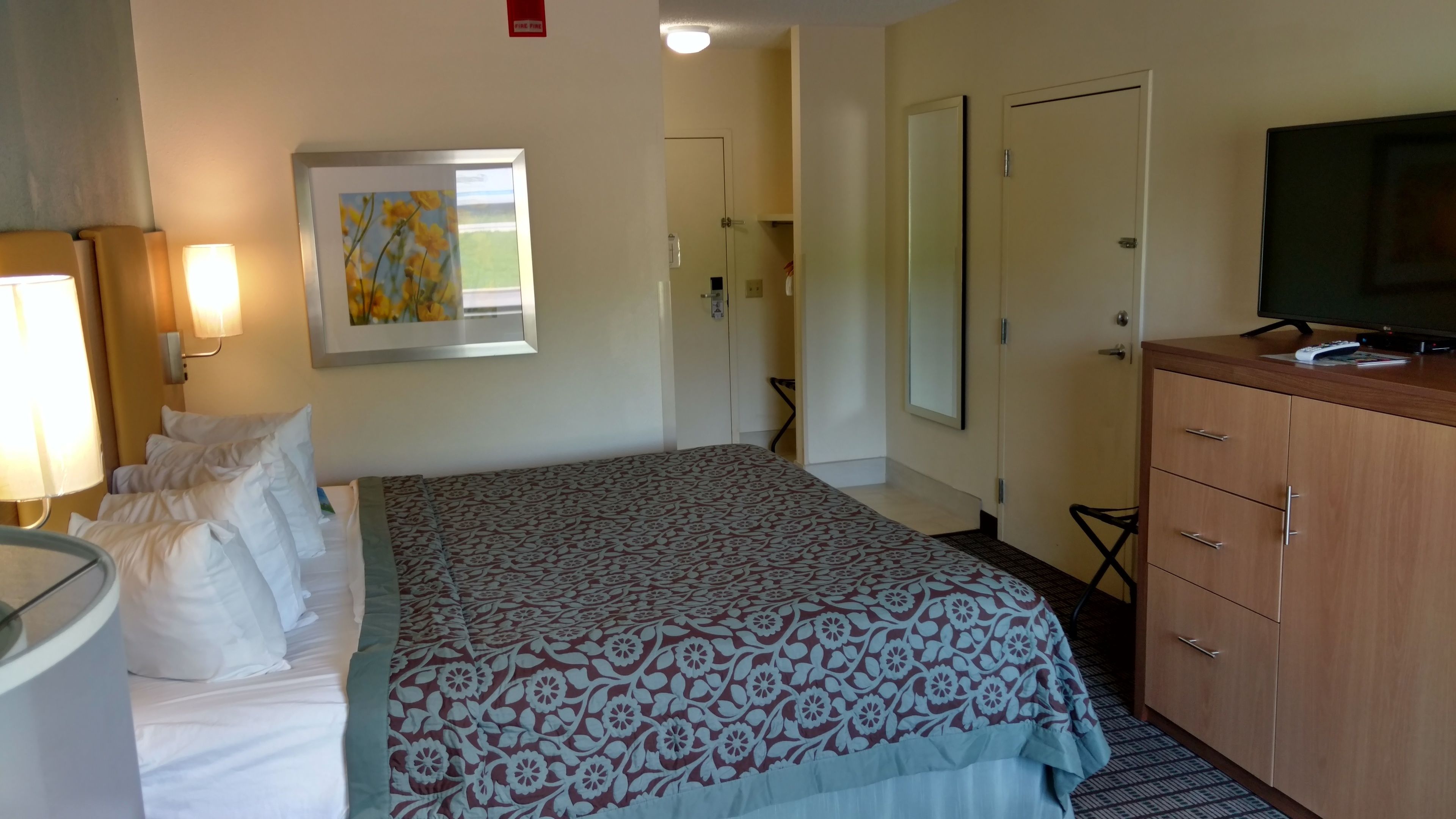 A hotel room with a bed, a television, a dresser, and a framed picture on the wall.