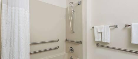 A bathroom with a shower, grab bars, a toilet, and a towel rack.