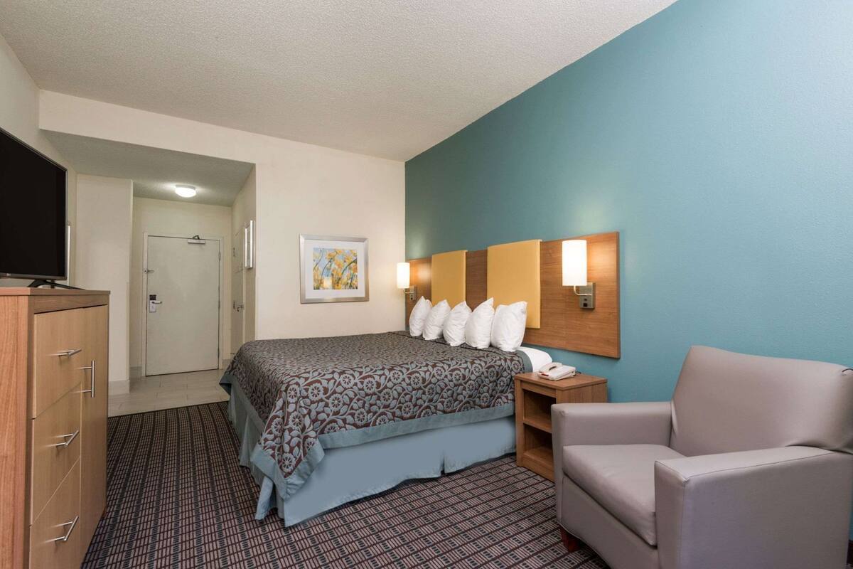 A hotel room with a bed, a desk, a chair, a television, and a door.