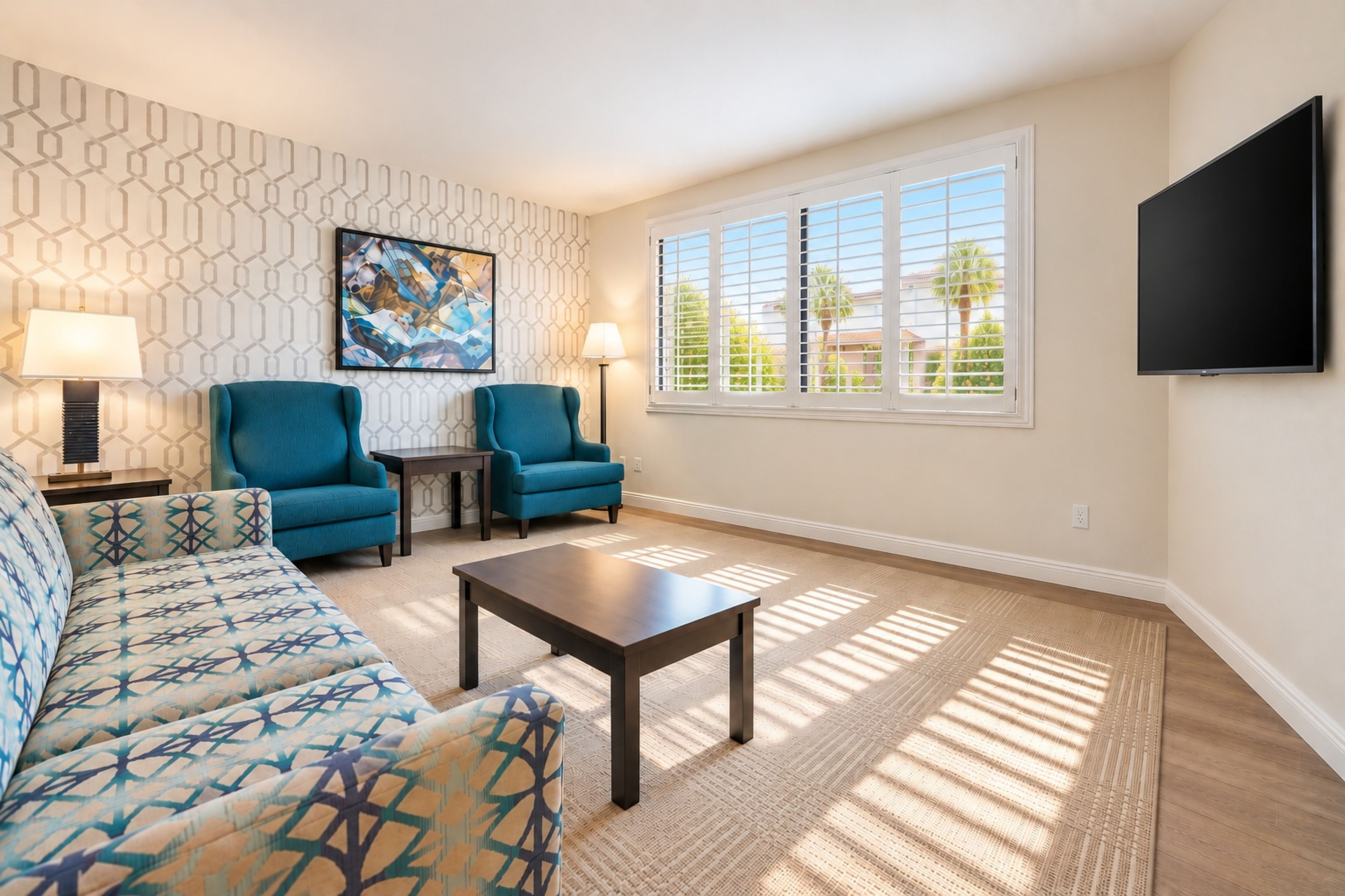 A living room with a patterned wall, two blue armchairs, a sofa, a coffee table, and a TV mounted on the wall.