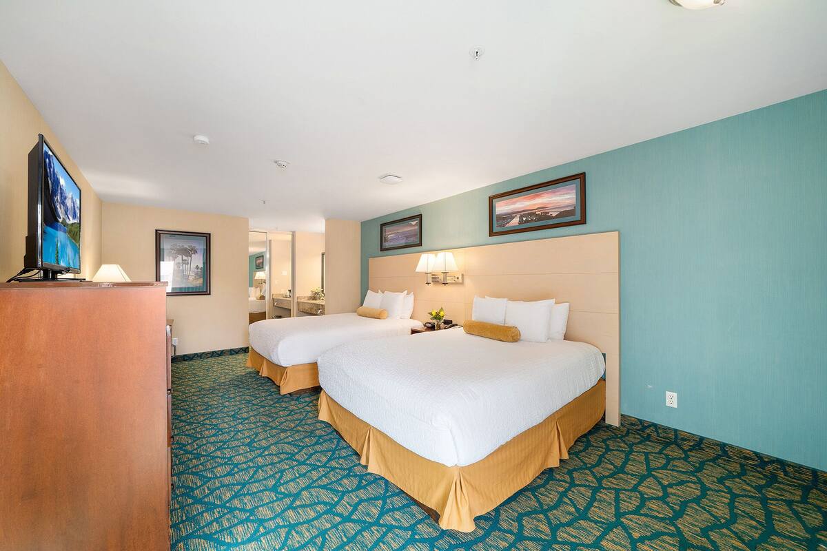 A hotel room with two beds, a desk, a TV, and a bathroom visible through an open door.