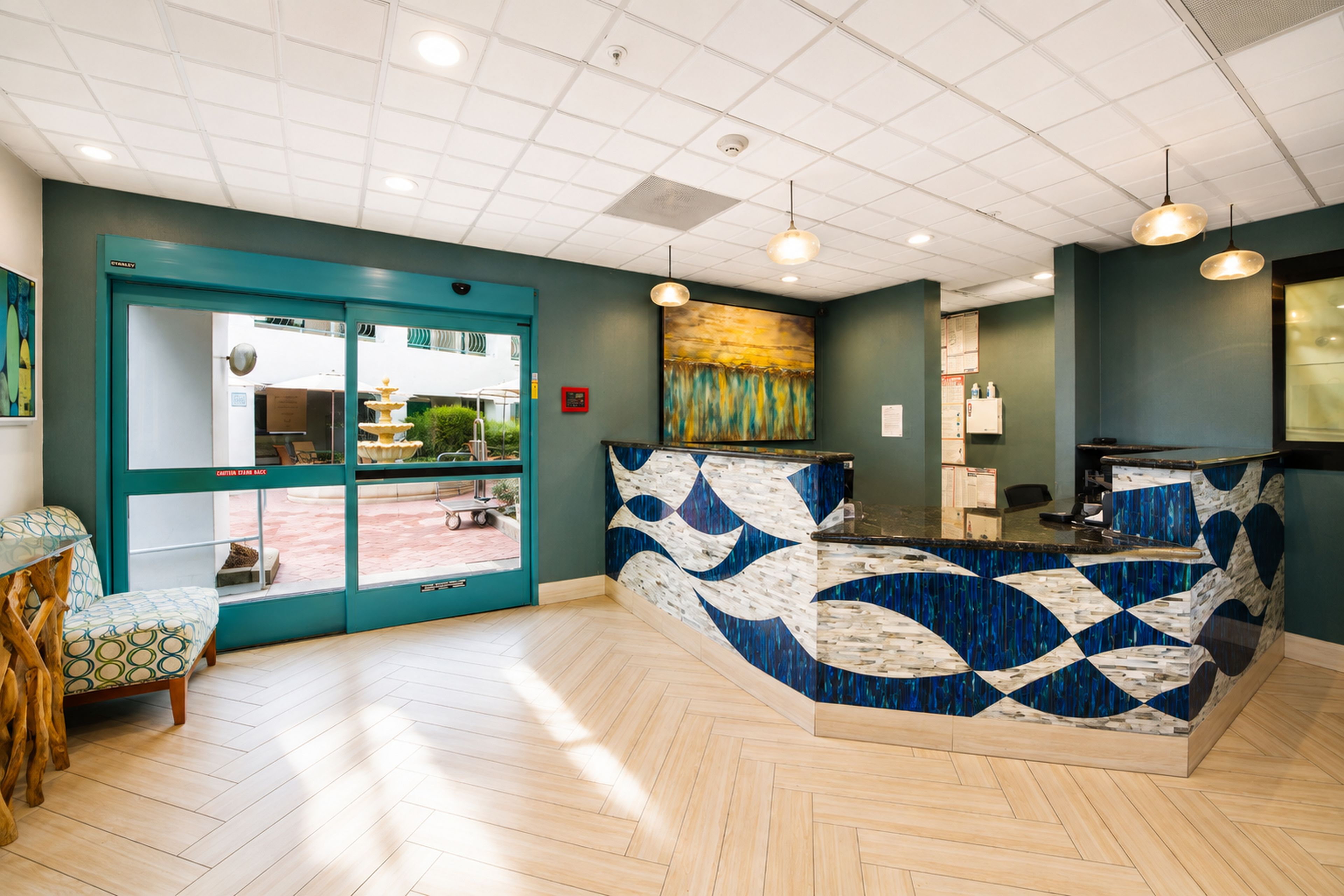 A reception area with a teal-colored desk, a glass door entrance, and a herringbone-patterned floor.