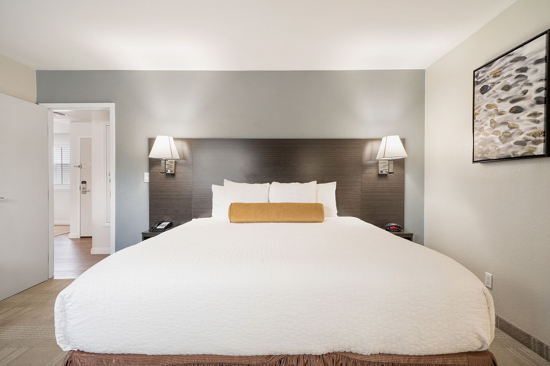 A hotel room with a large bed, two bedside lamps, a nightstand with a phone, and a framed picture on the wall.