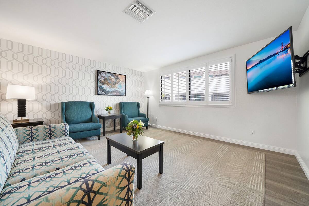 A modern living room with a sofa, two armchairs, a coffee table, and a flat-screen TV mounted on the wall.