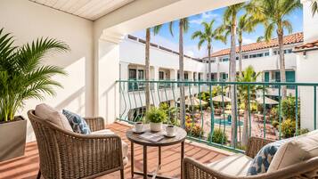 A balcony with wicker furniture, a small table, and a view of a pool and buildings.