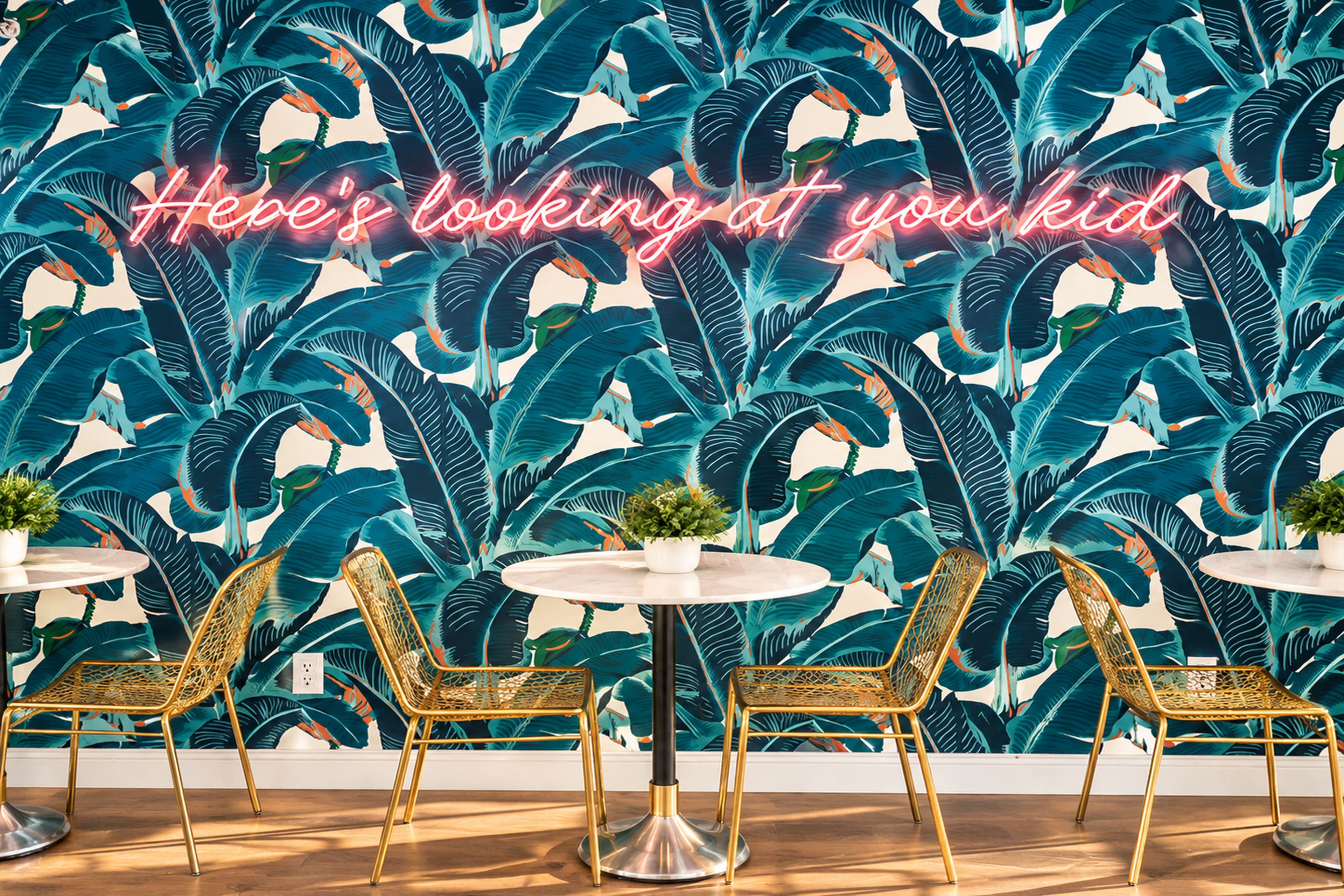 A room with a vibrant tropical leaf wallpaper, three round tables with chairs, and a neon sign.