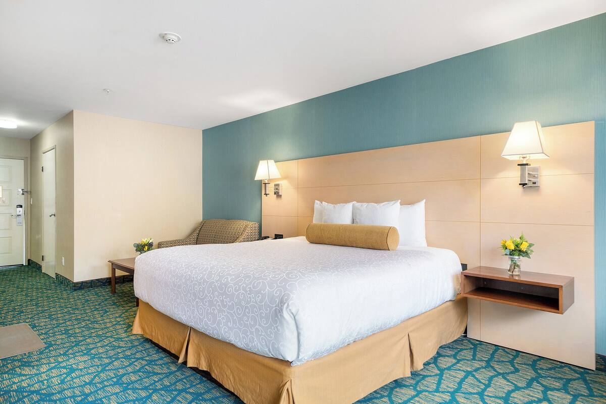 A hotel room with a large bed, two bedside tables with lamps, a small desk with a lamp, and a door.