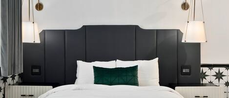 Une chambre d’hôtel moderne avec un grand lit, une tête de lit sombre, des tables de chevet et des lampes fixées au mur.