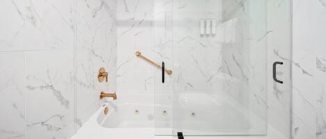 A modern bathroom with a glass-enclosed shower, marble walls, and gold fixtures.