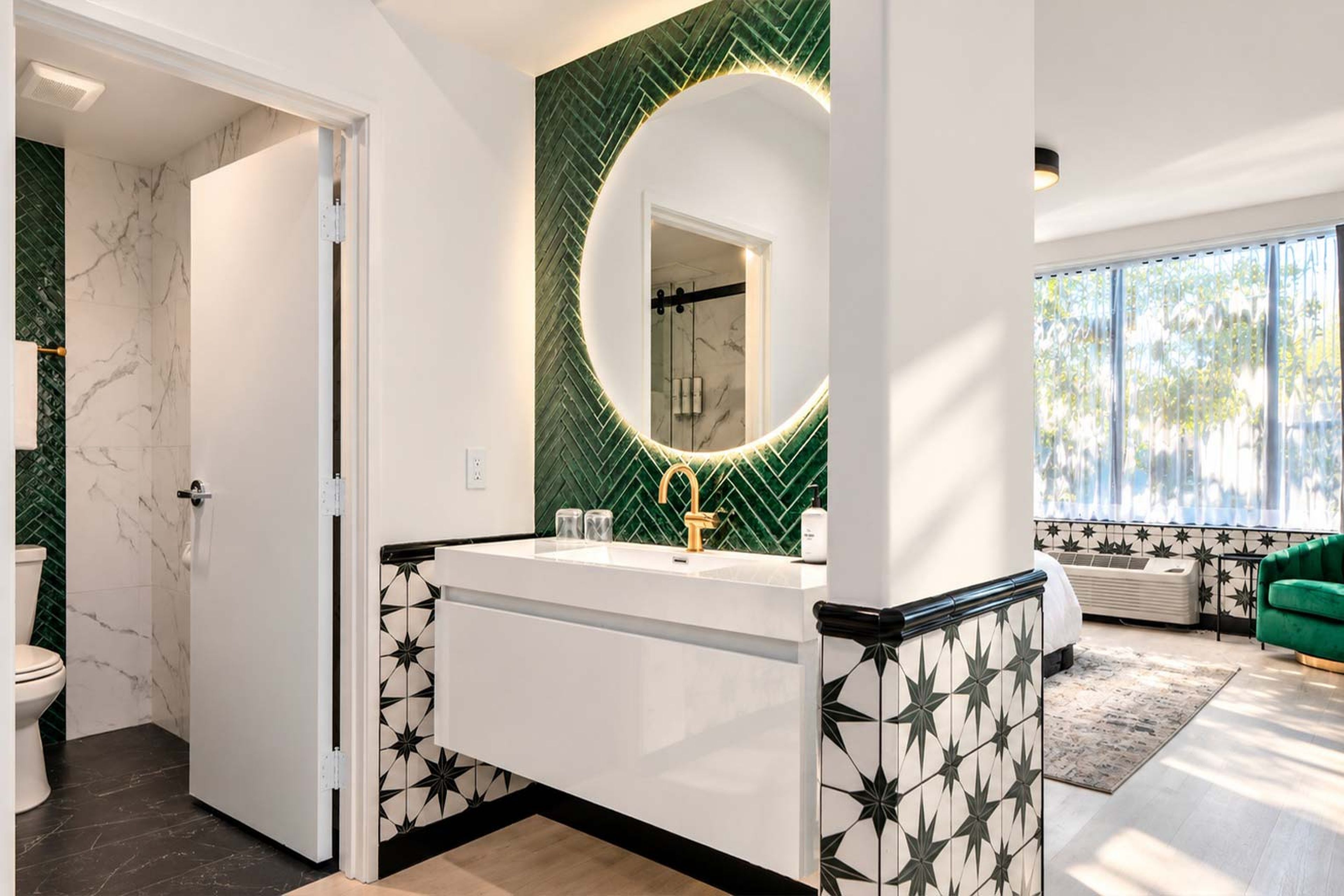 A modern bathroom with a white vanity, a gold faucet, and a green herringbone-patterned wall.