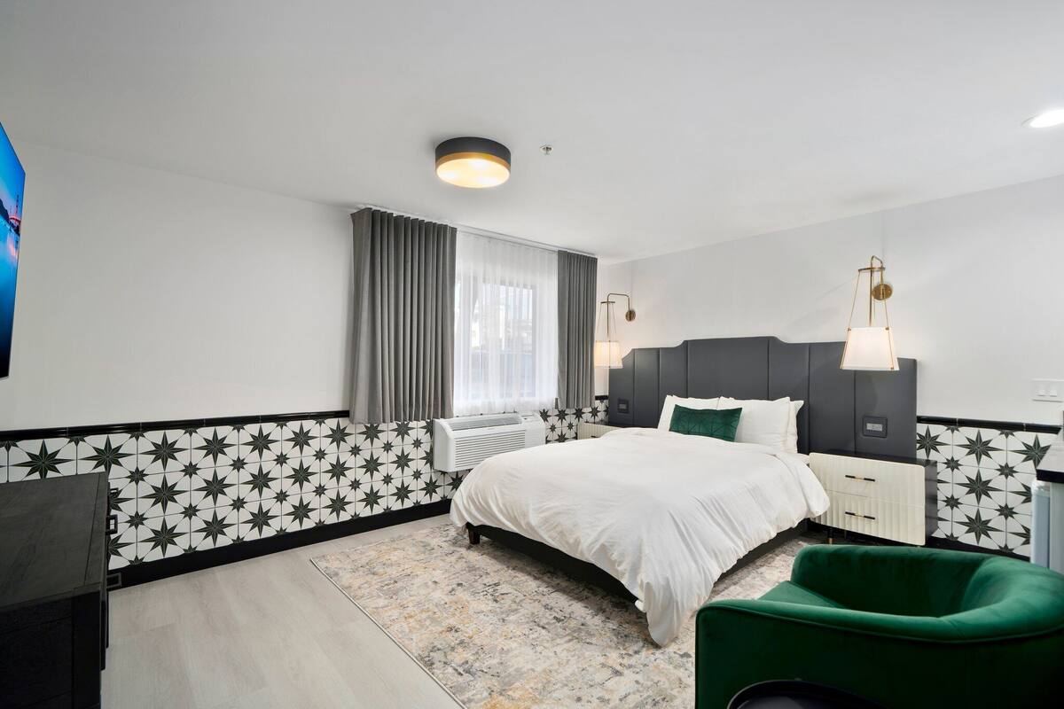 A modern hotel room with a large bed, a desk, a chair, and a window with curtains.