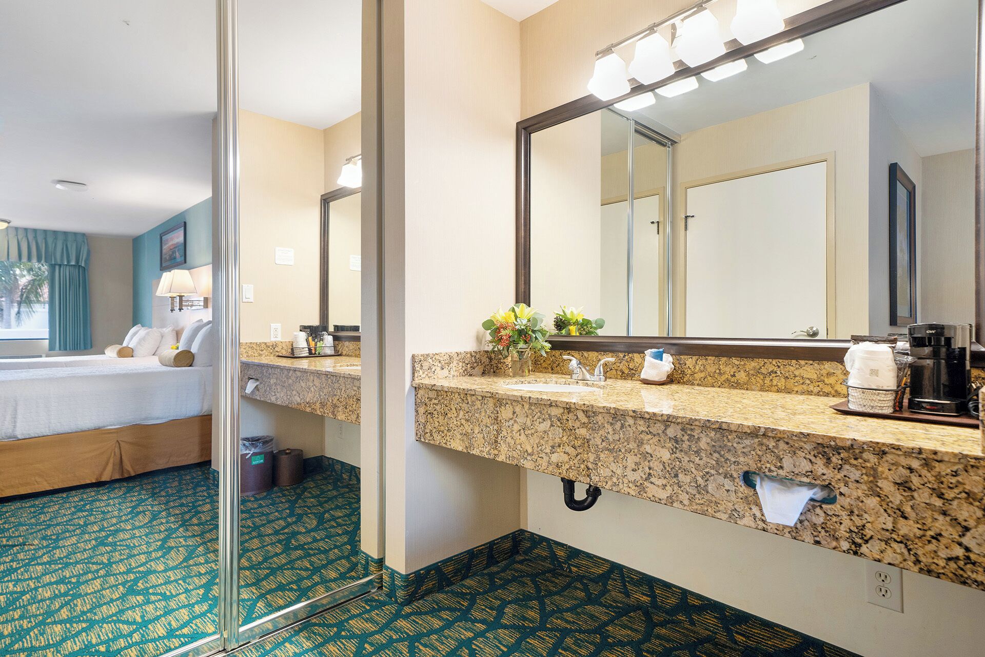 A hotel bathroom with a granite countertop, a large mirror, and a coffee machine.