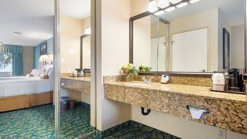 A hotel bathroom with a granite countertop, a large mirror, and a coffee machine.
