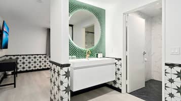 A modern bathroom with a white vanity, a green-tiled wall, and a marble shower area.