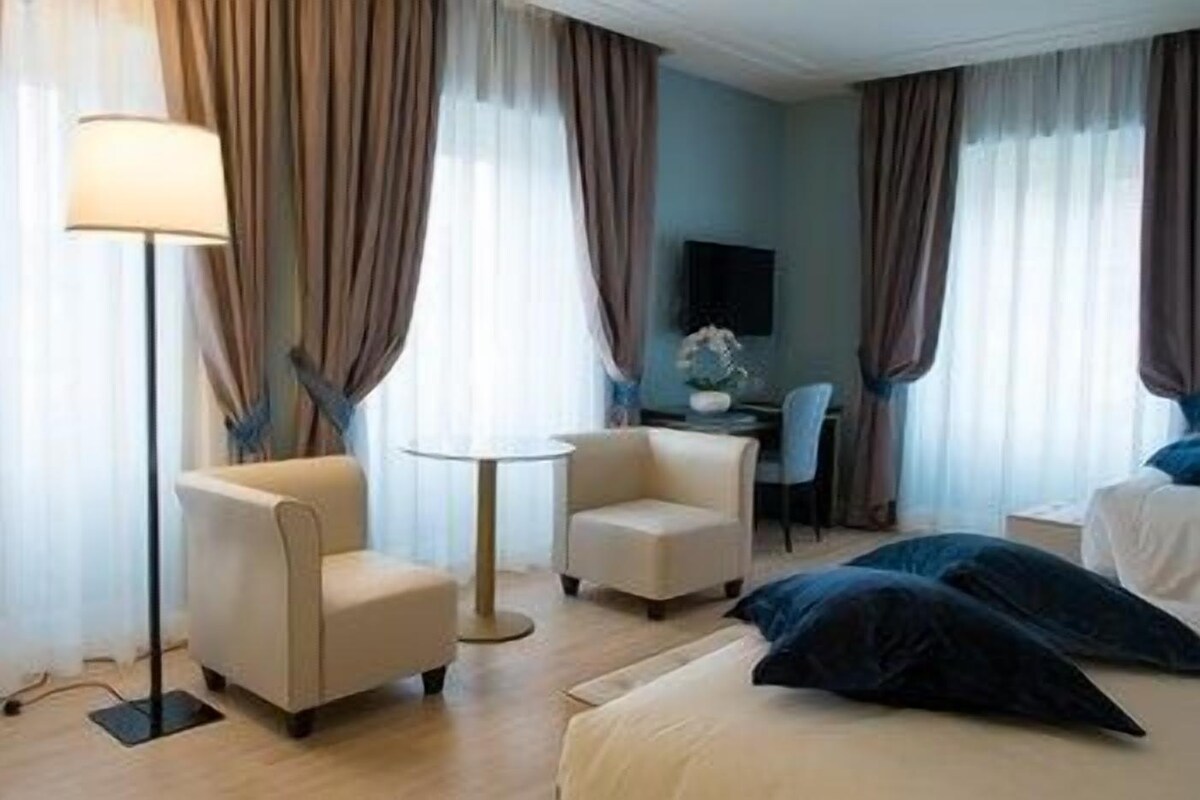 A hotel room with a bed, two armchairs, a small round table, a desk, and a lamp.