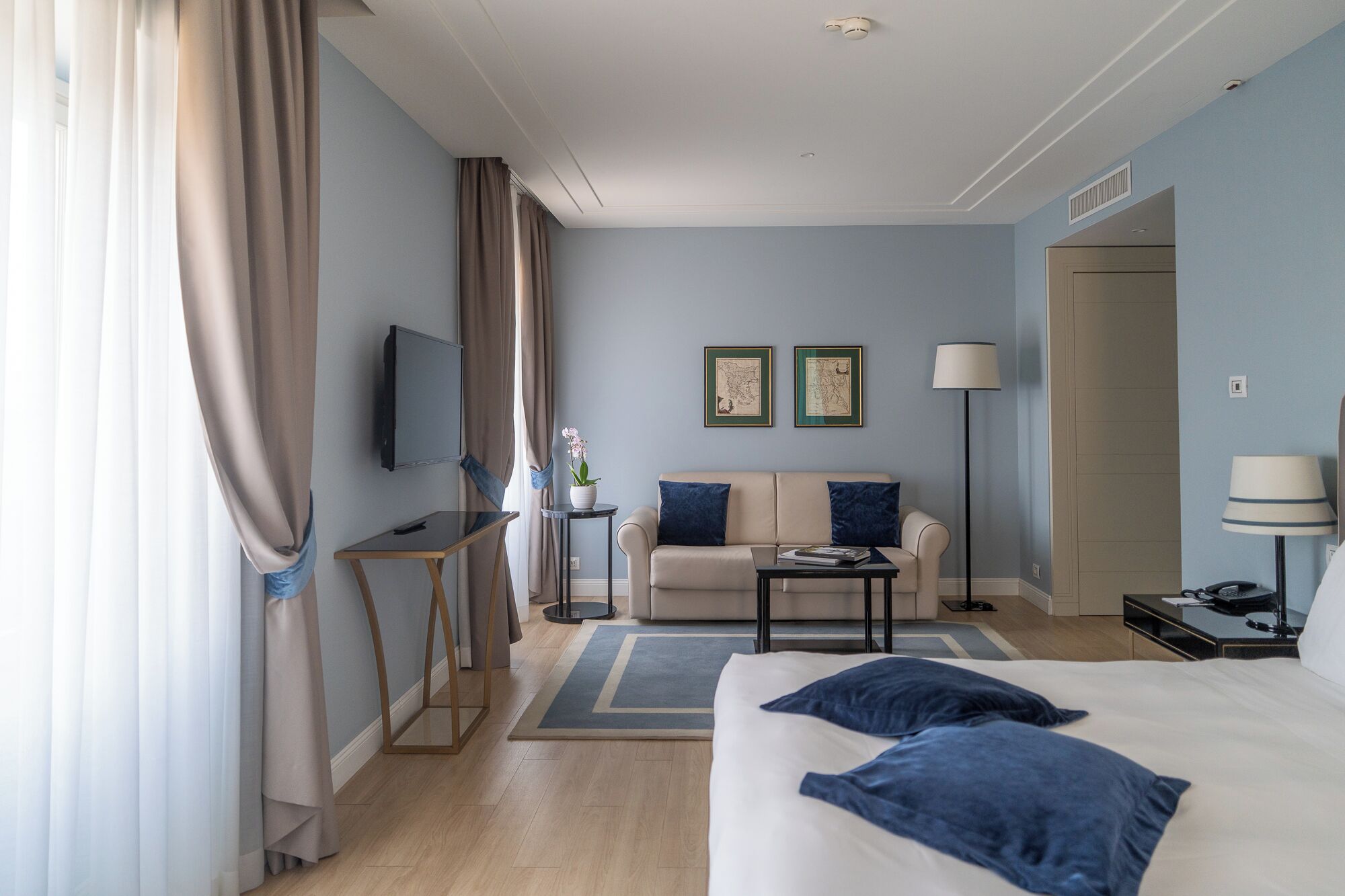 Ein Hotelzimmer mit Bett, Sofa, Fernseher, Schreibtisch und Lampe.