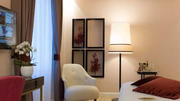 Habitación de hotel con cama, escritorio con un florero, una silla, lámpara y cuadros en la pared.