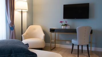 Habitación de hotel con cama, escritorio con televisor de pantalla plana, dos sillas, lámpara y pequeña mesa con flores.