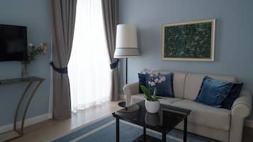 Un soggiorno moderno con un divano, un tavolino, una TV, una lampada e un quadro appeso al muro.