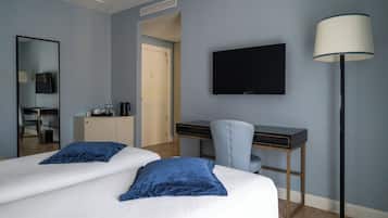 A hotel room with two beds, a desk, a chair, a TV, and a lamp.