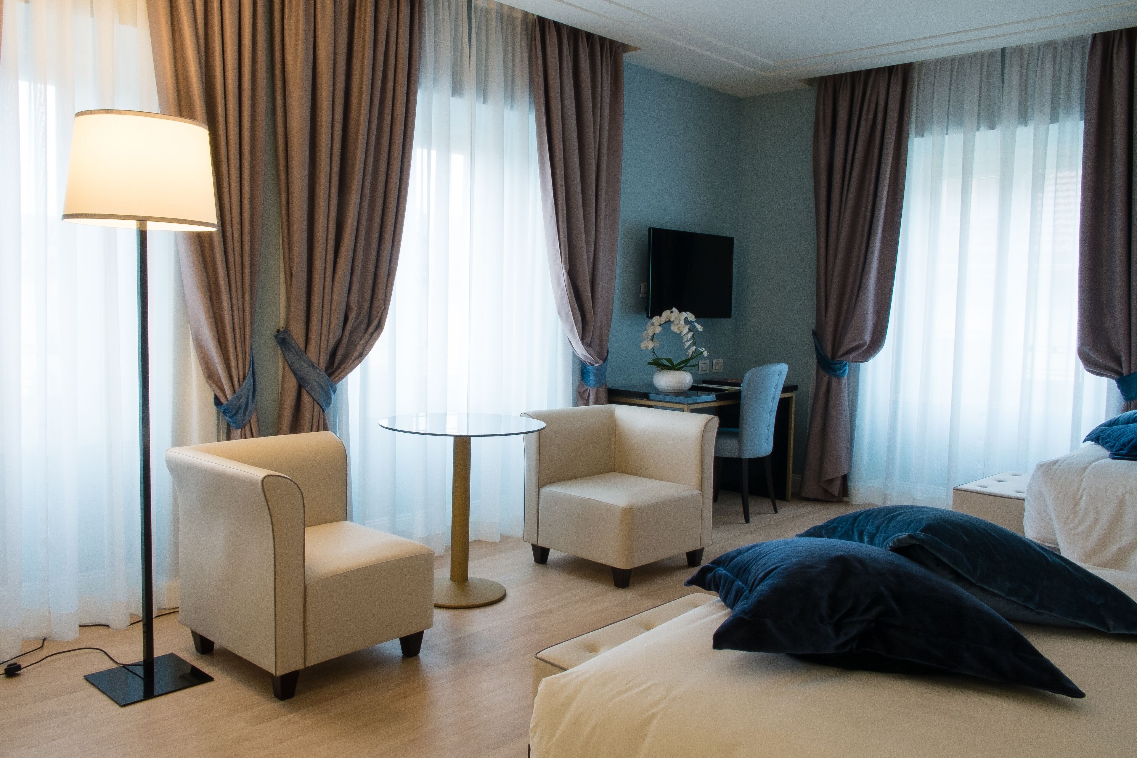 Una habitación de hotel con cama, dos sillones, un escritorio, una lámpara y cortinas.