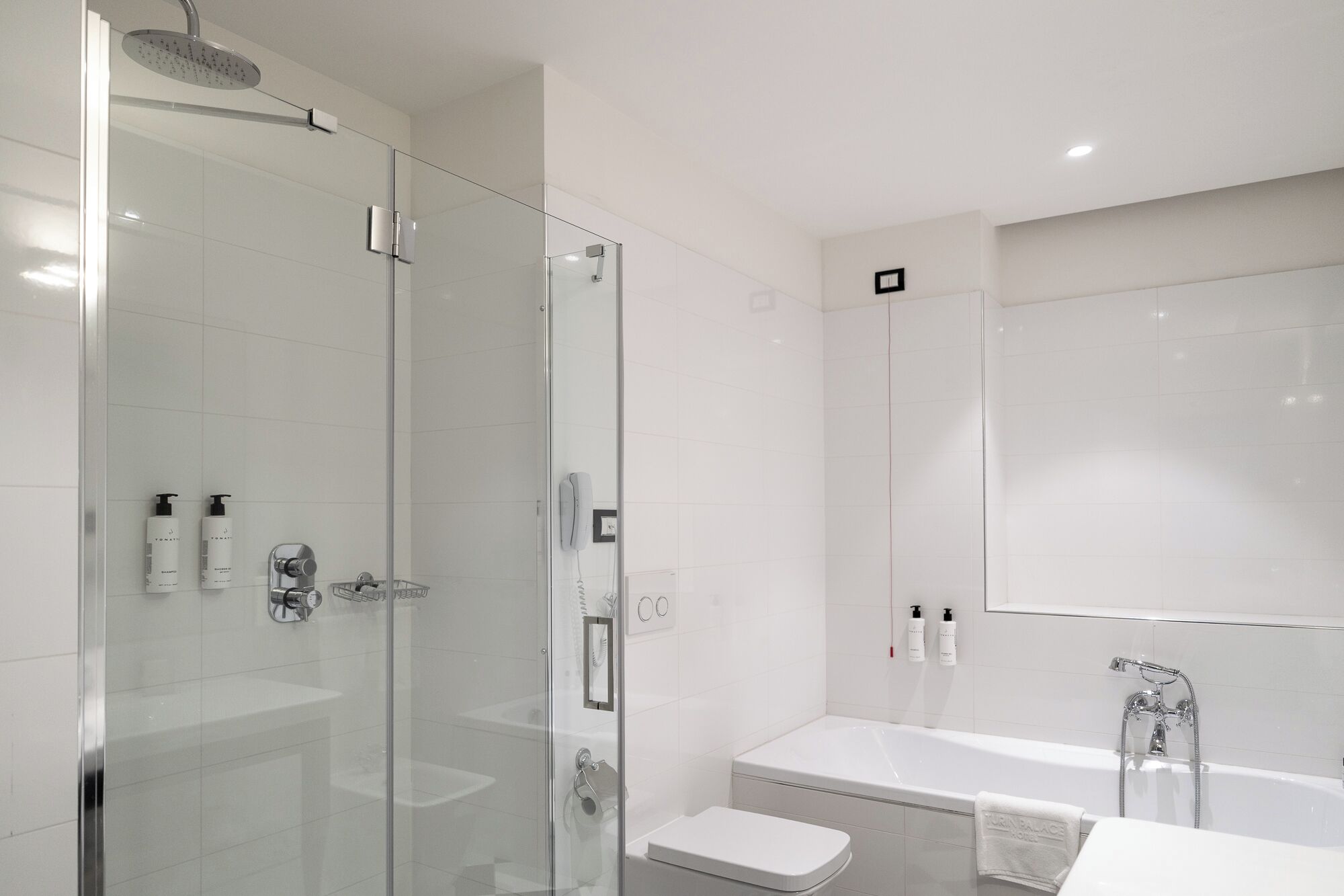 Un baño moderno con ducha de vidrio, inodoro blanco, bañera y un espejo grande.