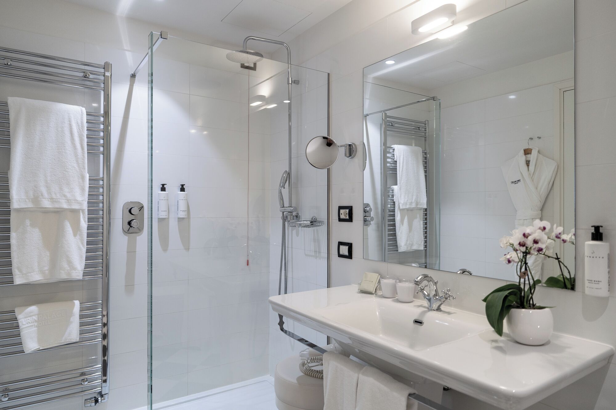 A modern bathroom with a glass-enclosed shower, a large mirror, a white sink, and a towel rack.