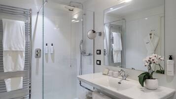 A modern bathroom with a glass-enclosed shower, a large mirror, a white sink, and a towel rack.