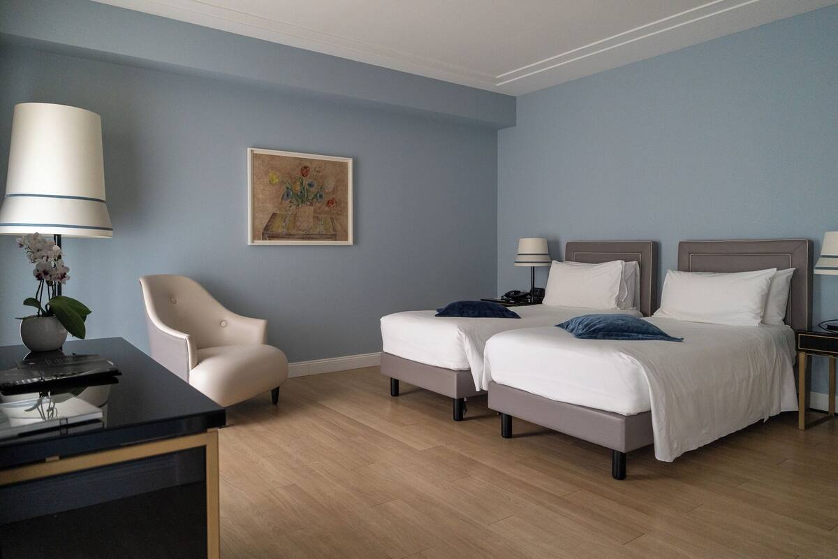 Une chambre d’hôtel avec deux lits, un bureau, une chaise et un tableau au mur.