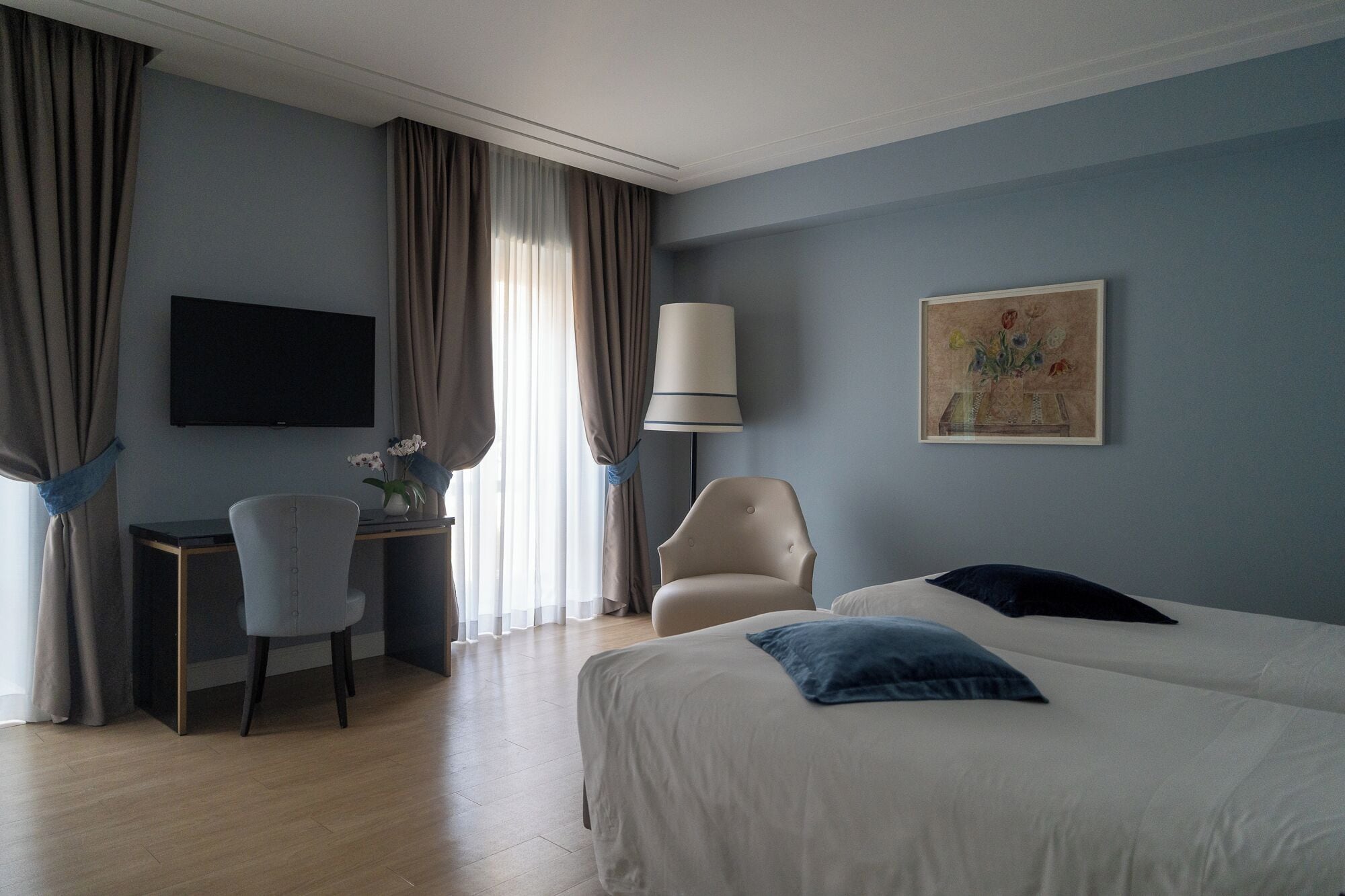 Una habitación de hotel con cama, escritorio, silla, televisor y un cuadro en la pared.