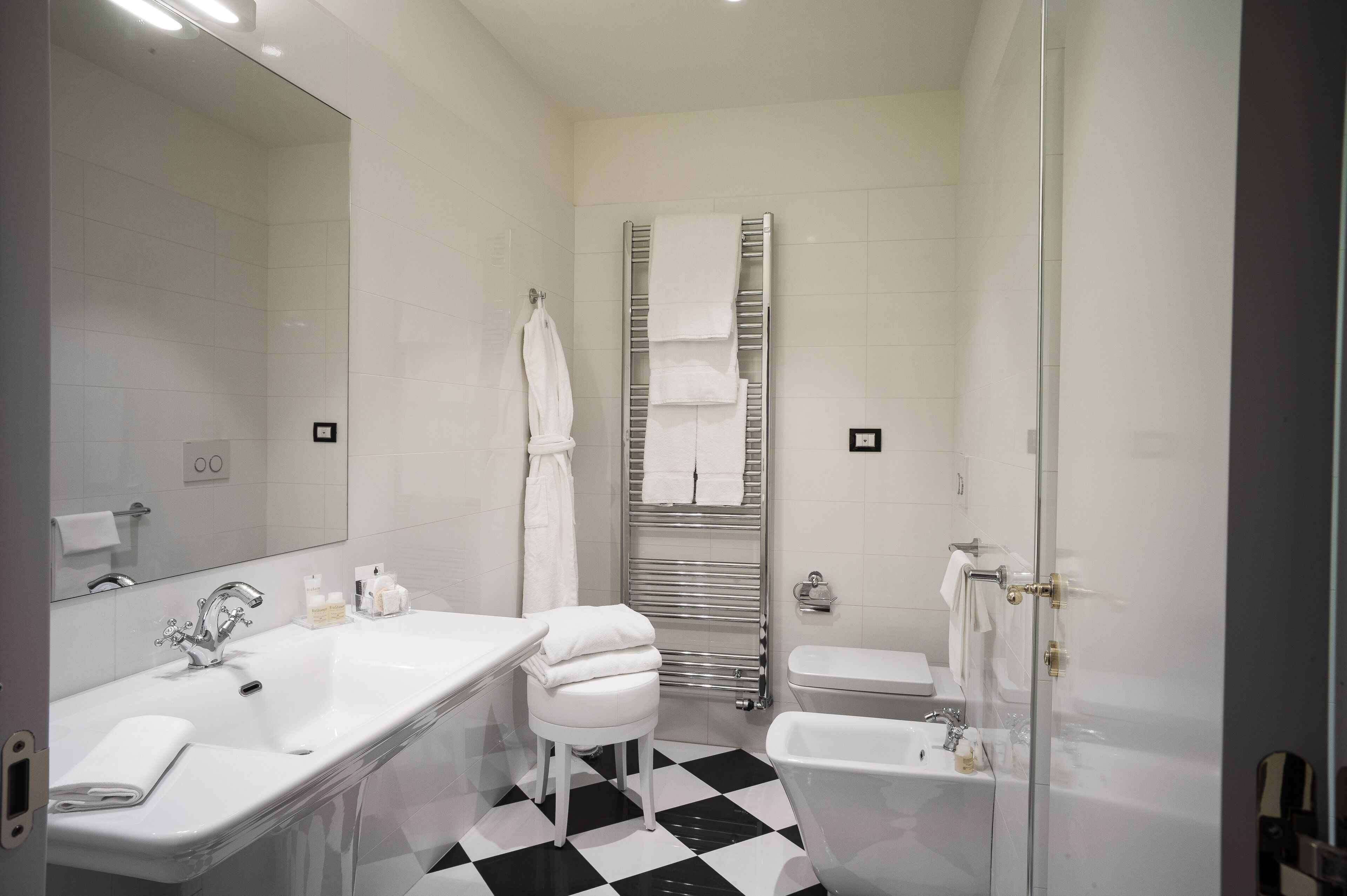 Een moderne badkamer met een witte wastafel, spiegel en een zwart-wit geruite vloer.