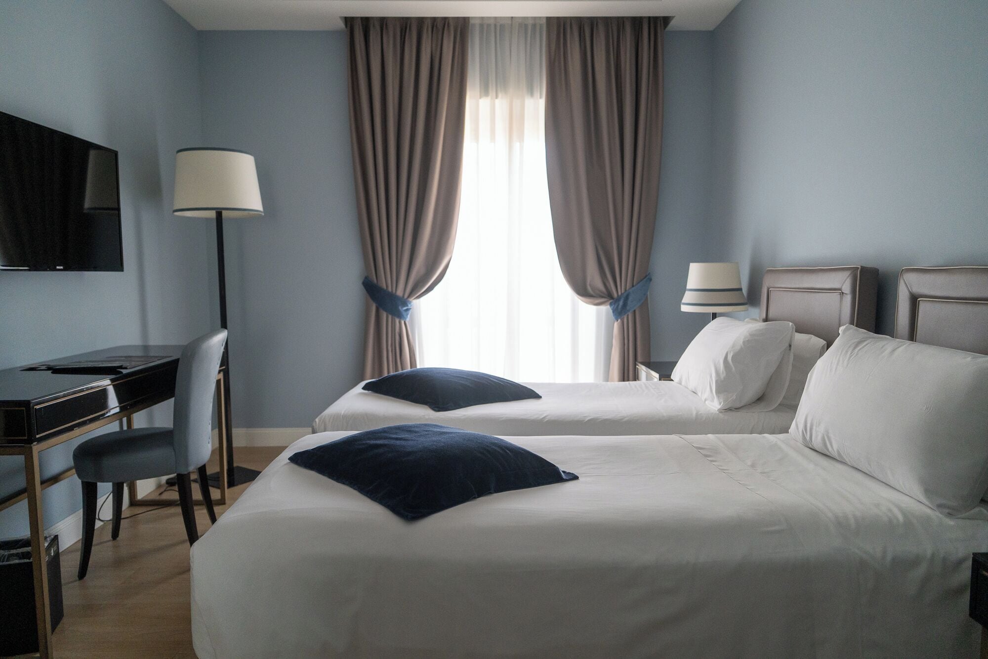Habitación de hotel con dos camas, un escritorio, una silla, un televisor y una ventana con cortinas.