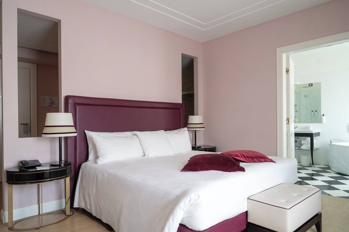 Une chambre d’hôtel avec un grand lit, deux tables de chevet, une petite table, un bureau et une chaise.