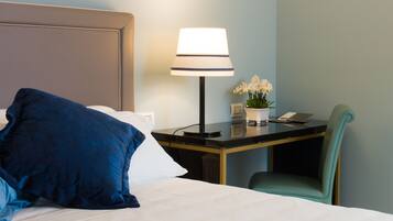 Quarto de hotel com cama, escrivaninha com luminária, cadeira e mesa pequena com planta e telefone.