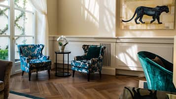 A room with two patterned armchairs, a small table with a plant, and a large painting on the wall.